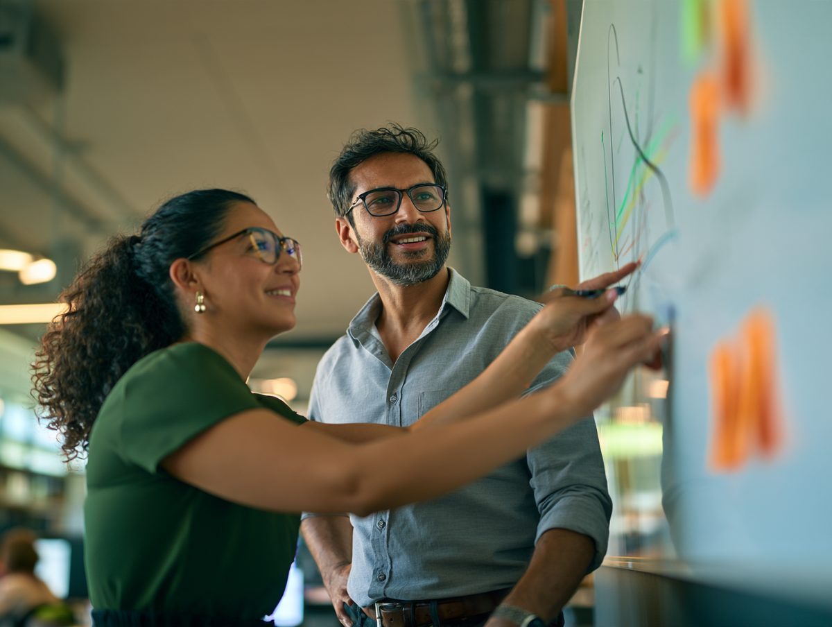 Two market analysts sketching supply and demand curves on a whiteboard